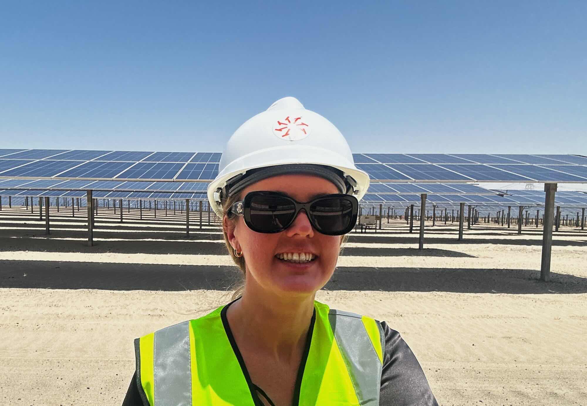 Engineer in safety gear visiting a solar power plant, standing in front of photovoltaic panels installed across a desert site.